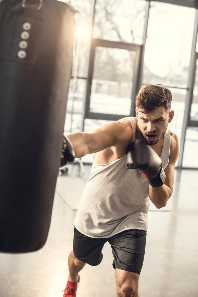 эмоциональная тренировка молодого спортсмена с боксерской грушей в спортзале
 - Фото, изображение