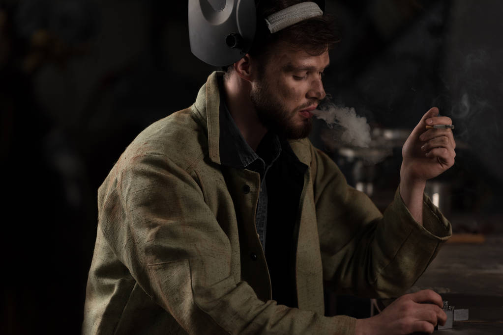 operaio con maschera protettiva sollevata seduto e fumare sigarette in fabbrica
  - Foto, immagini