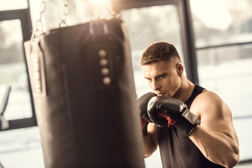 спортивний молодий чоловік в боксерських рукавичках тренування з ударною сумкою в спортзалі
 - Фото, зображення