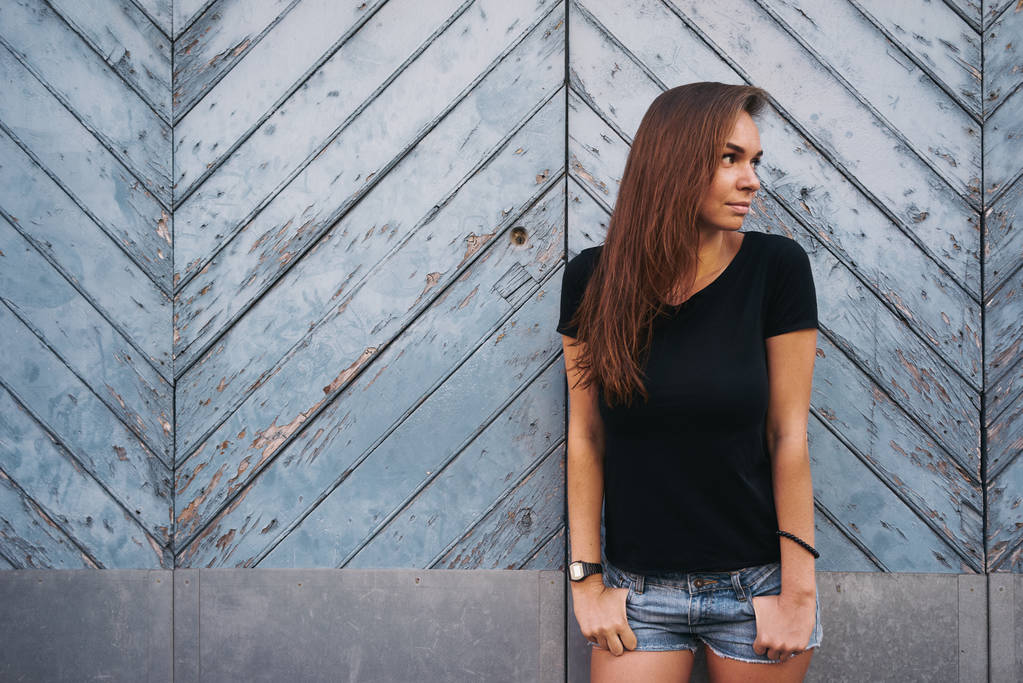 hafif mavi ahşap çit karşı bekleyen boş bir siyah t-shirt güzel genç kadın - Fotoğraf, Görsel