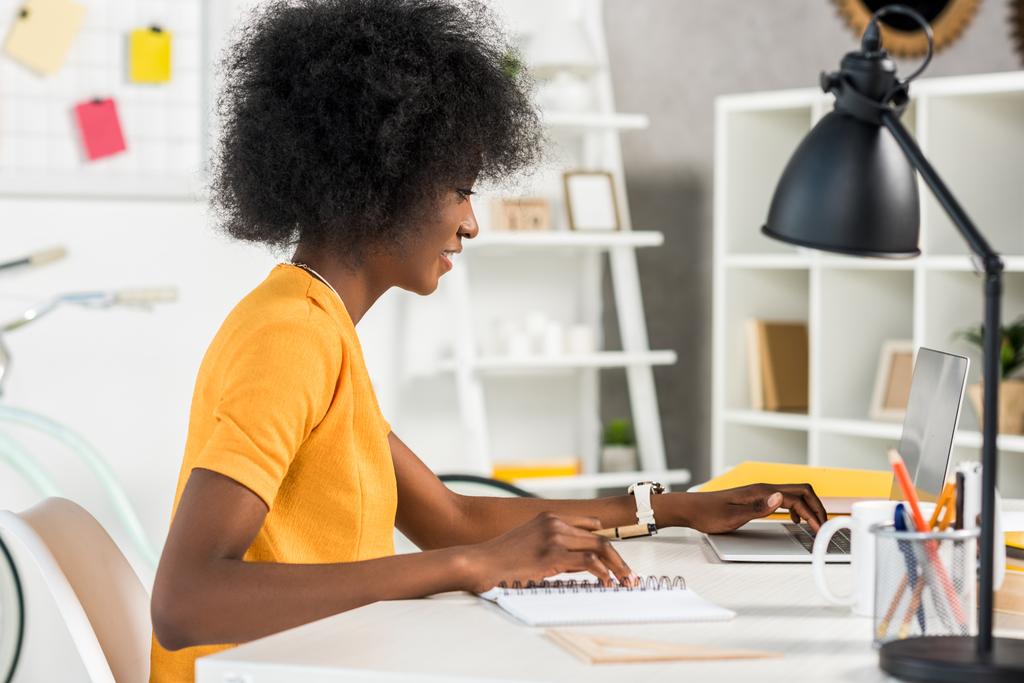 боковой вид африканского фрилансера, работающего на ноутбуке на рабочем месте дома
 - Фото, изображение