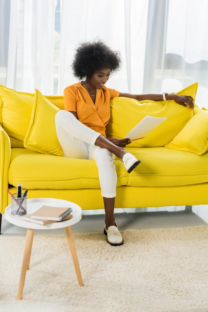 hymyilevä afrikkalainen amerikkalainen nainen paperit kauko työskentelee sohvalla kotona
 - Valokuva, kuva