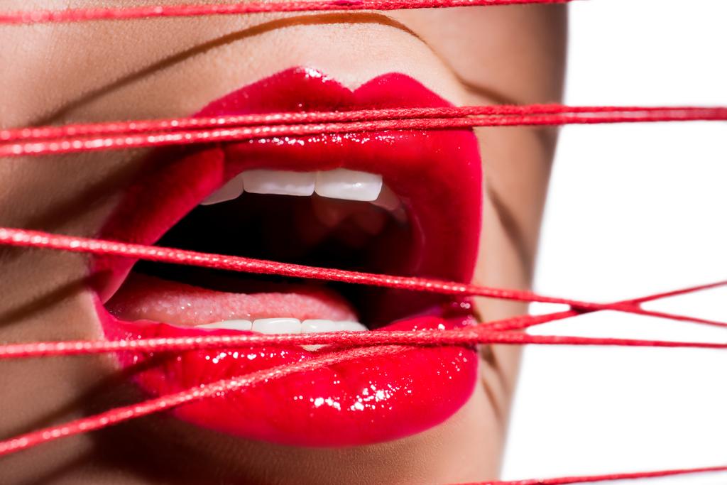 imagem cortada de mulher com batom vermelho e boca aberta tocando fios vermelhos isolados em branco
 - Foto, Imagem
