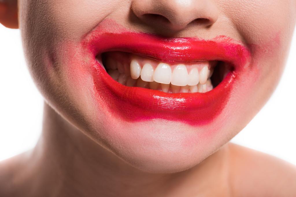 abgeschnittenes Bild einer Frau mit verschmiertem roten Lippenstift im Gesicht, die Zähne isoliert auf Weiß zeigt - Foto, Bild