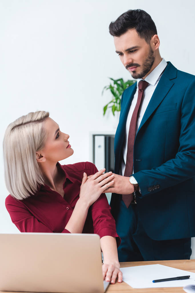 молодий чоловік і жінка бізнес-колеги тримають руки і дивляться один на одного в офісі
 - Фото, зображення