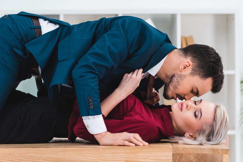 вид сбоку на сексуальную молодую пару, целующуюся на столе в офисе
 - Фото, изображение