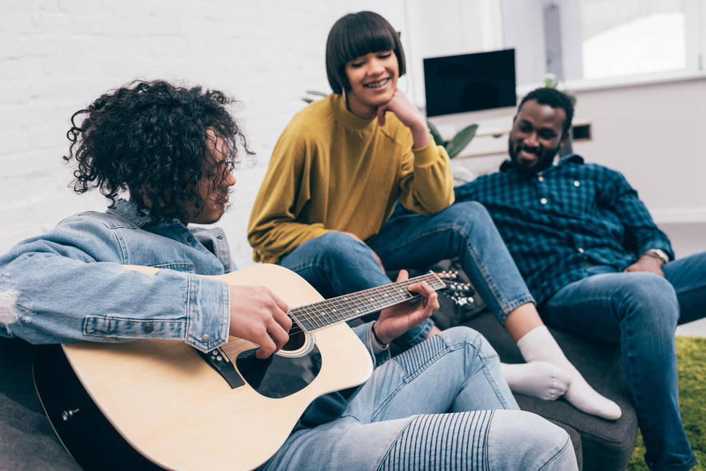 vista lateral de la raza mixta joven tocando la guitarra a amigos multiculturales
  - Foto, imagen