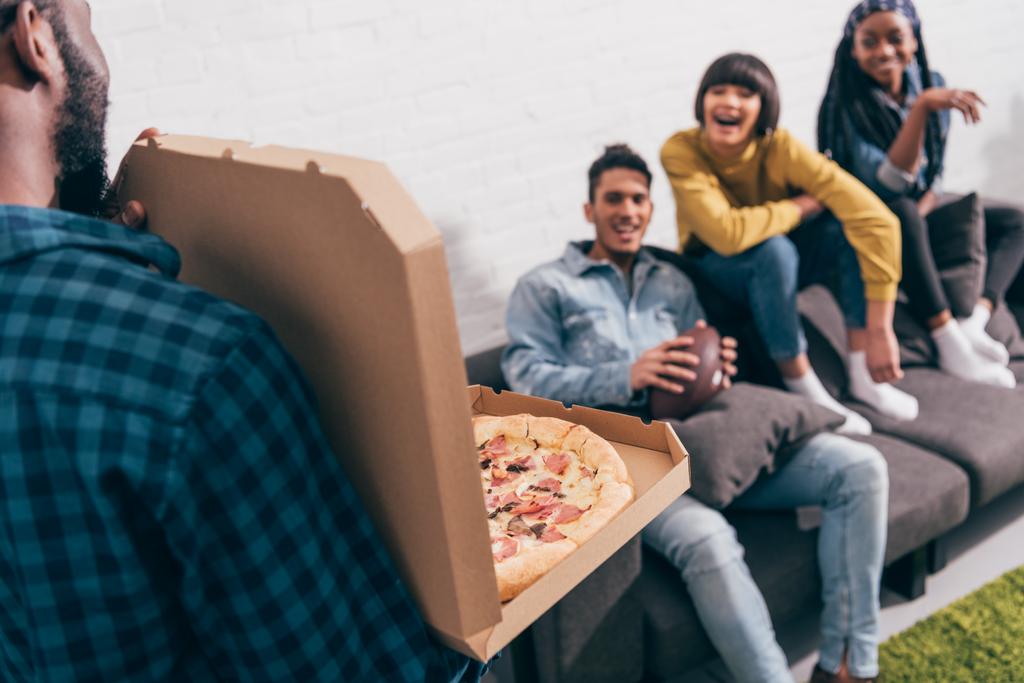 image recadrée de jeune homme noir montrant boîte à pizza à des amis sur le canapé
 - Photo, image