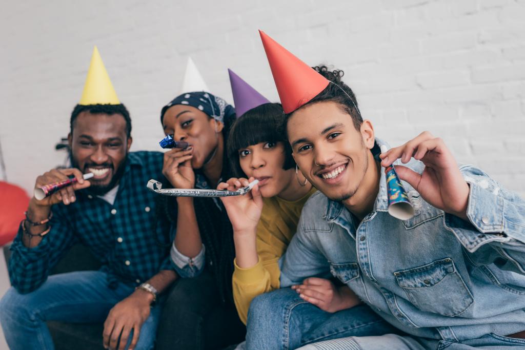 jeunes amis multiethniques dans des chapeaux de fête célébrant avec des cornes de fête
  - Photo, image