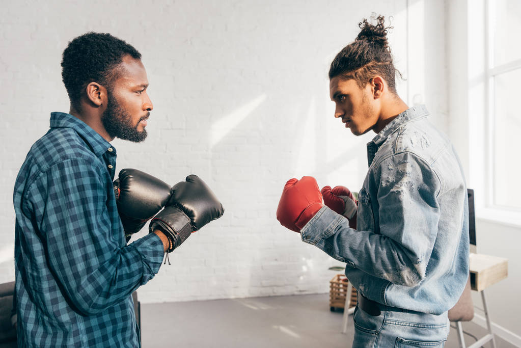 Zijaanzicht van twee multiculturele jonge mannen boksen met handschoenen  - Foto, afbeelding