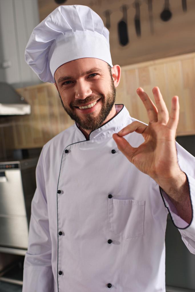 Lächelnder männlicher Koch zeigt Ok-Zeichen auf Küche - Foto, Bild