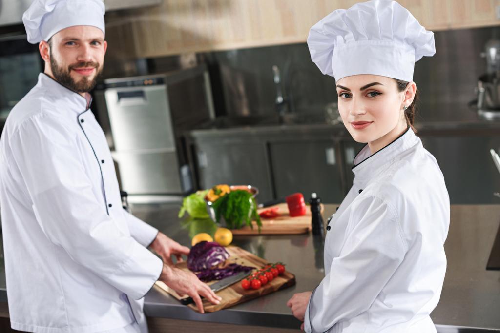 Професійні кухарі дивляться на камеру за столом з інгредієнтами приготування їжі
 - Фото, зображення