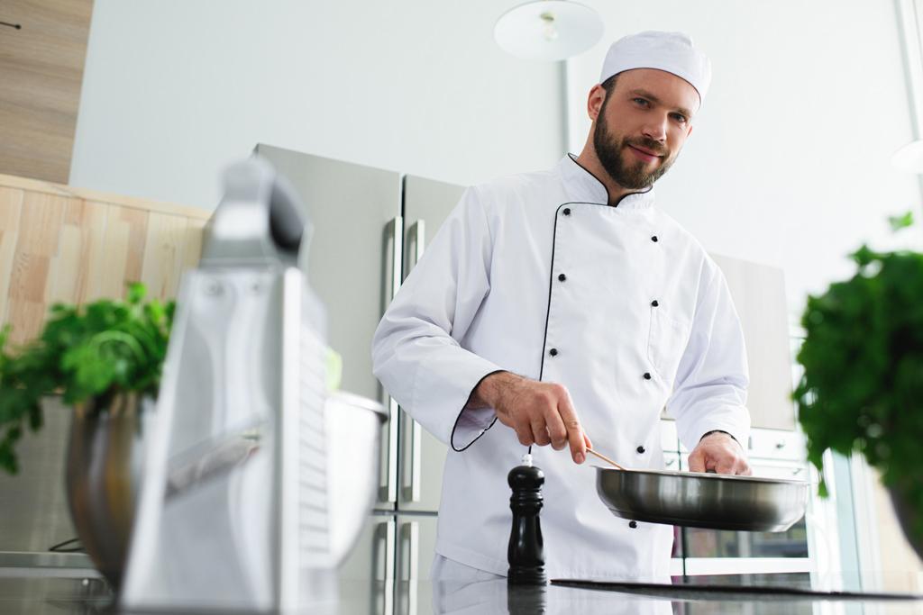 низький кут зору красивого шеф-кухаря смажать овочі на сковороді на кухні ресторану
 - Фото, зображення