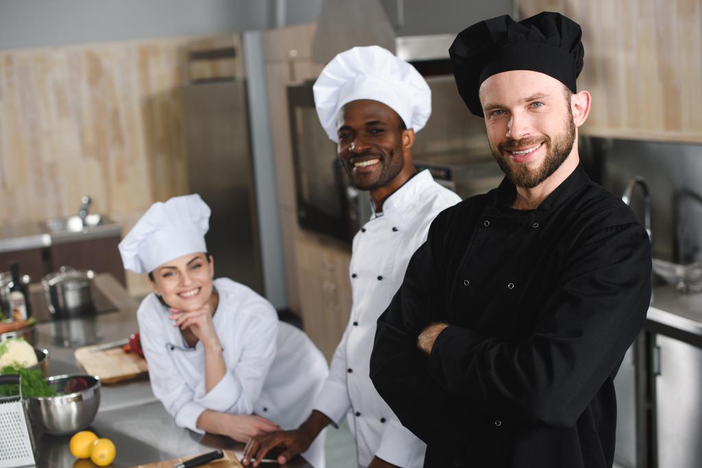 uśmiechający się wielokulturowym kucharzy, patrząc na kamery w restauracji kitchen - Zdjęcie, obraz