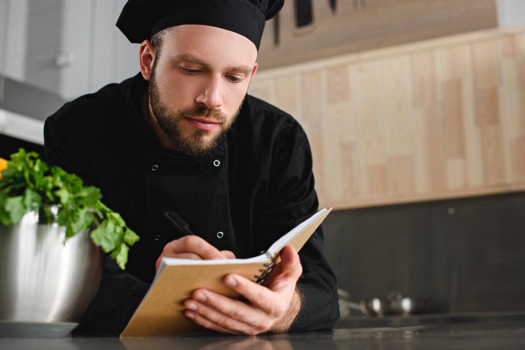 hezký šéfkuchař napíše nový recept na Poznámkový blok v restauraci kitchen - Fotografie, Obrázek
