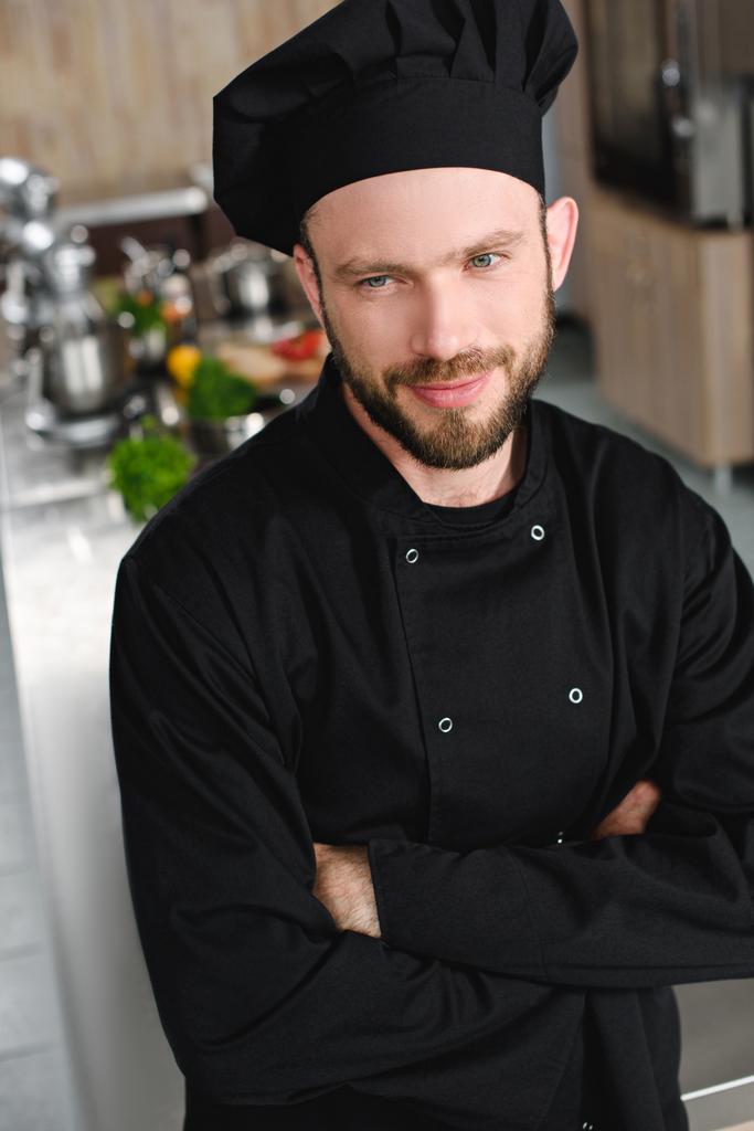 guapo chef de pie con los brazos cruzados y mirando a la cocina del restaurante
 - Foto, Imagen
