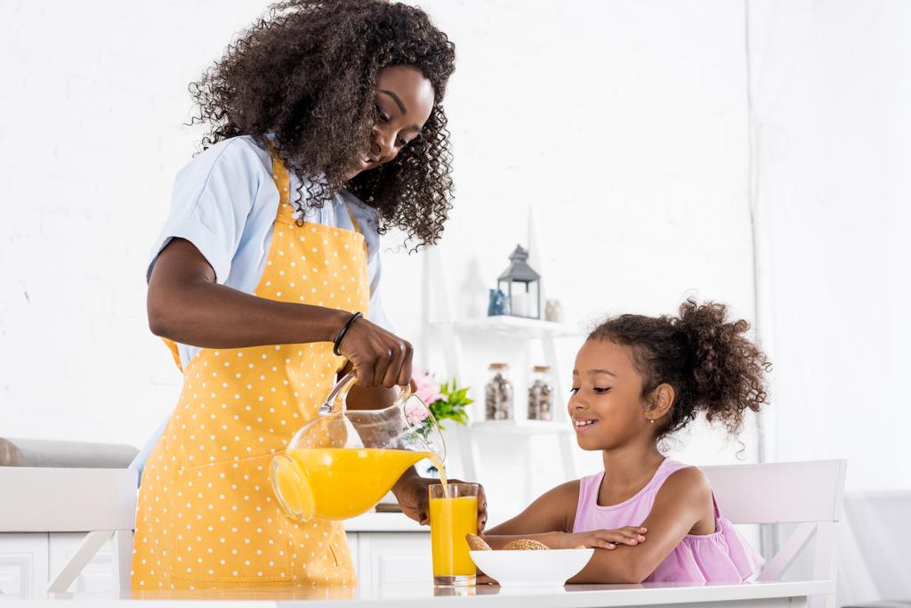 afro-américaine mère et fille dans des tabliers avec du jus d'orange sur la cuisine
 - Photo, image