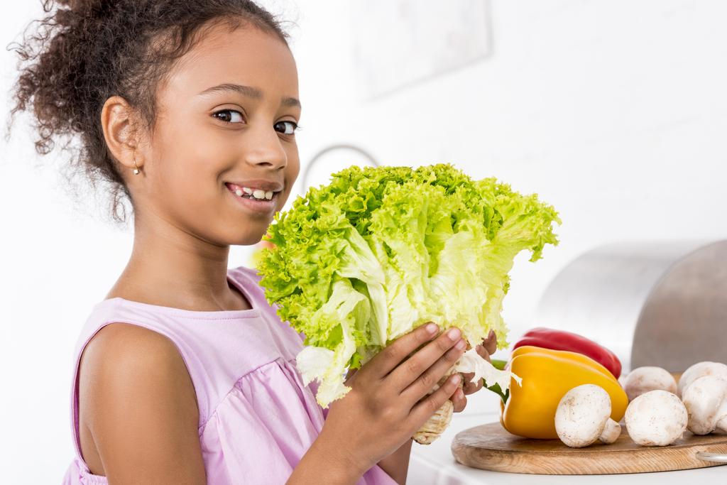 hymyilevä afrikkalainen amerikkalainen lapsi tilalla vihreä tuore salaatti keittiössä
 - Valokuva, kuva