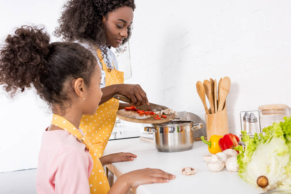 african american mother and daughter putting ingredientes in saucepan on kitchen - Photo, Image