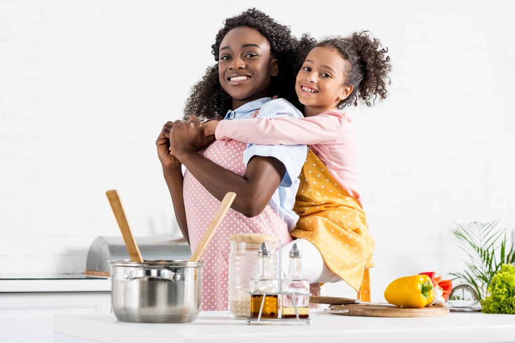 ευτυχισμένη μητέρα αφρικανική αμερικανική piggybacking κόρη στην κουζίνα - Φωτογραφία, εικόνα