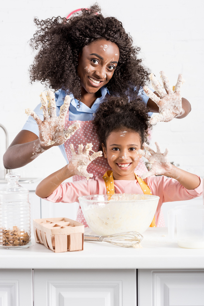 Африканский американец мать и забавная дочь показывая руки в тесте на кухне
 - Фото, изображение