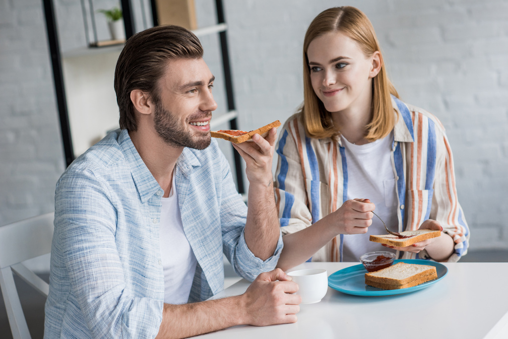 jovem casal comer torradas com geléia durante o café da manhã à mesa
  - Foto, Imagem