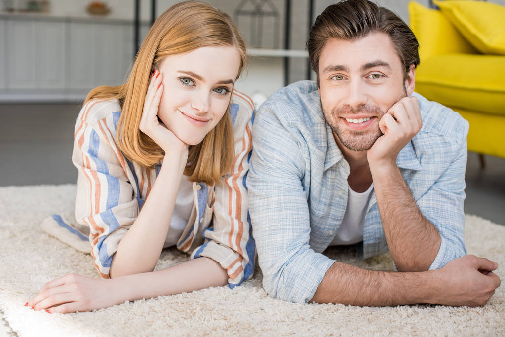 junges lächelndes Paar liegt auf Teppich im Wohnzimmer - Foto, Bild
