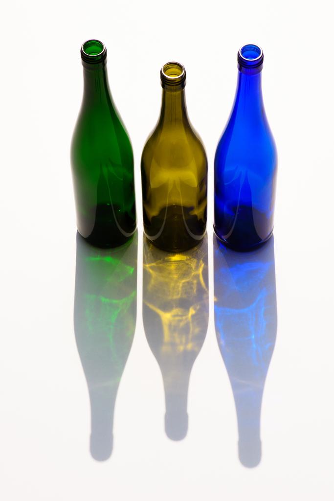 vista de perto de garrafas de vidro coloridas vazias com sombras no fundo branco
 - Foto, Imagem