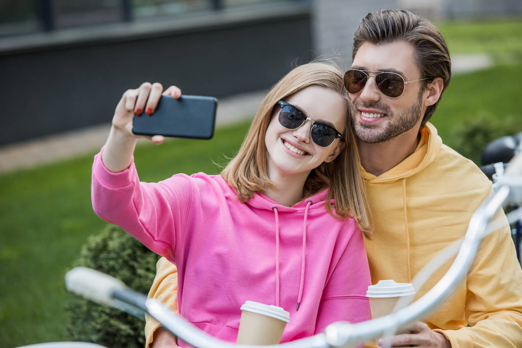 hymyilevä nuori nainen aurinkolasit ottaen selfie poikaystävän kanssa
  - Valokuva, kuva