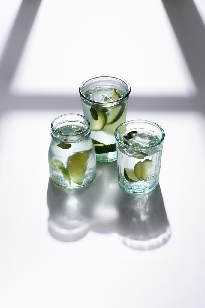 close up view of glasses with water, lime pieces and ice cubes on white tabletop - Photo, Image
