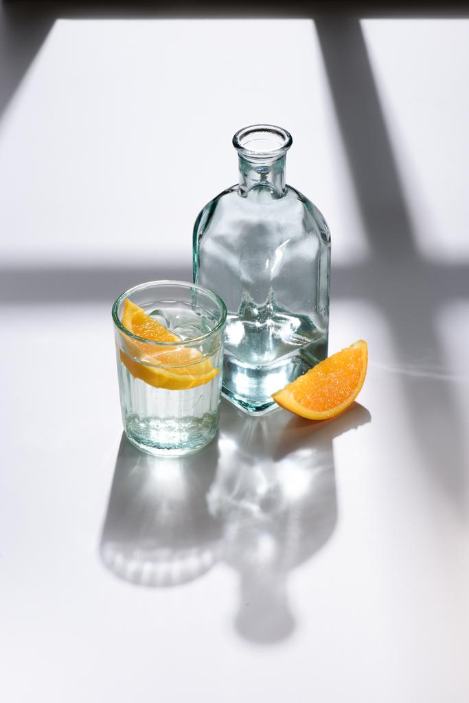 close up view of glass, lemon pieces and bottle with water on white surface - Photo, Image