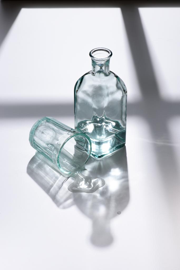 Nahaufnahme von leeren Glas und Flasche mit Wasser auf weißer Oberfläche - Foto, Bild