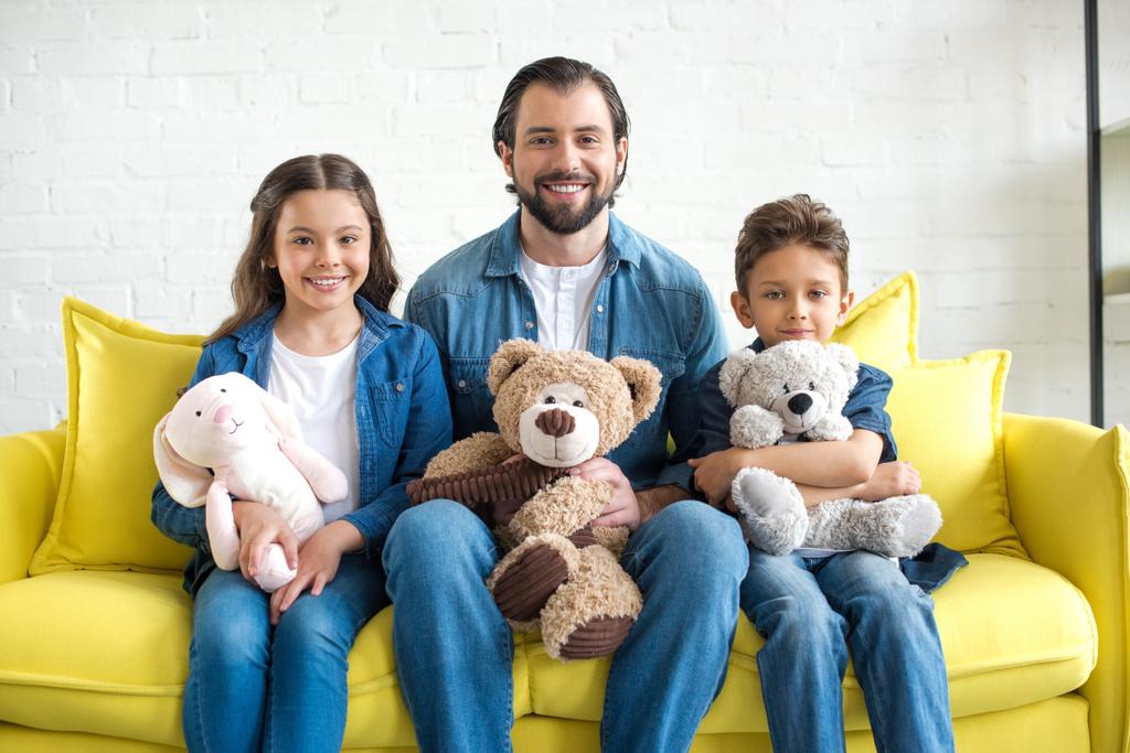 щасливий батько з двома чарівними дітьми тримає іграшки і посміхається на камеру вдома
 - Фото, зображення