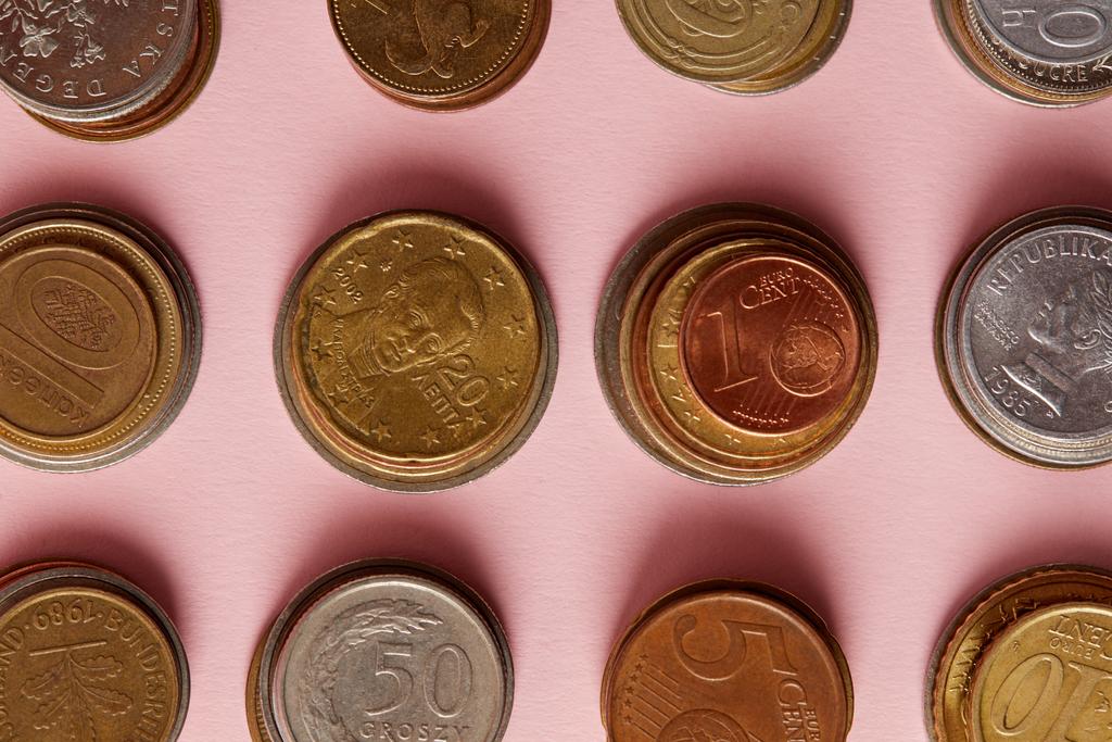 вид сверху стопок монет из разных стран на розовом фоне
 - Фото, изображение