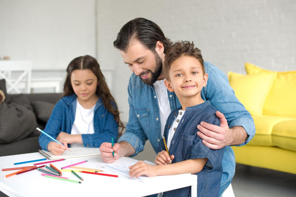 щасливий батько і двоє чарівних дітей малюють кольоровими олівцями вдома
 - Фото, зображення
