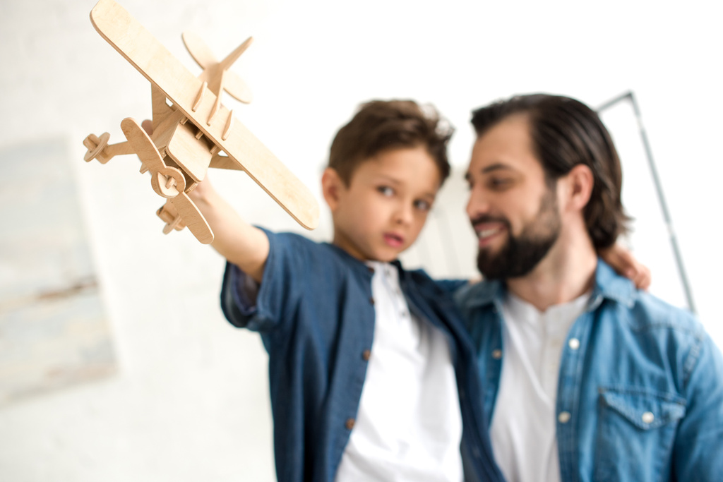 крупным планом отец и сын играют с деревянным игрушечным самолетом
 - Фото, изображение