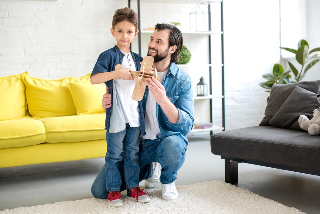 pai feliz e pequeno filho brincando com avião de brinquedo de madeira em casa
  - Foto, Imagem