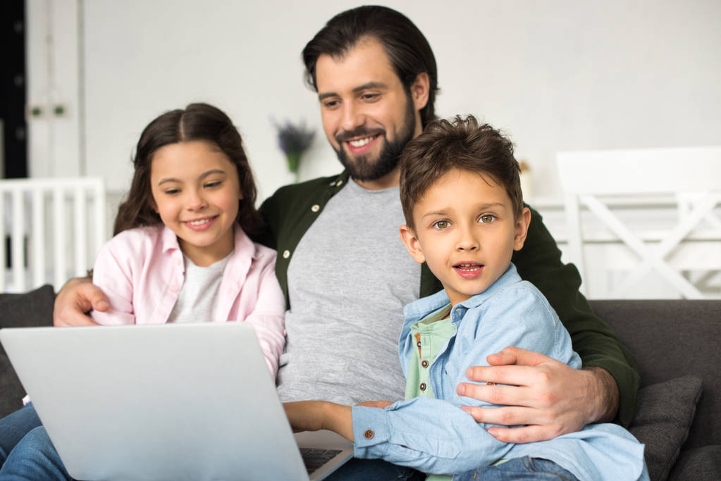 souriant père avec deux adorables enfants utilisant ordinateur portable ensemble à la maison
 - Photo, image