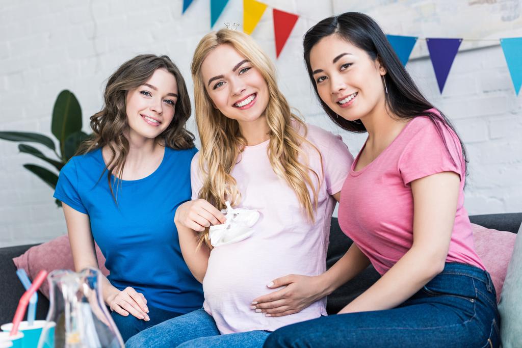 multicultural friends and pregnant woman with baby shoes looking at camera at baby-party - Photo, Image