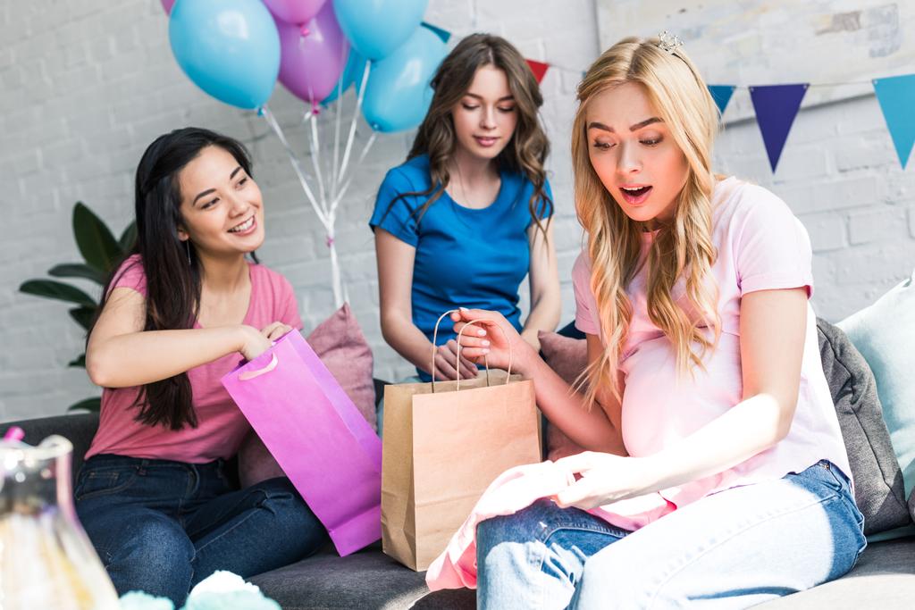 surprised pregnant woman looking at presents from multicultural friends on baby-party - Photo, Image