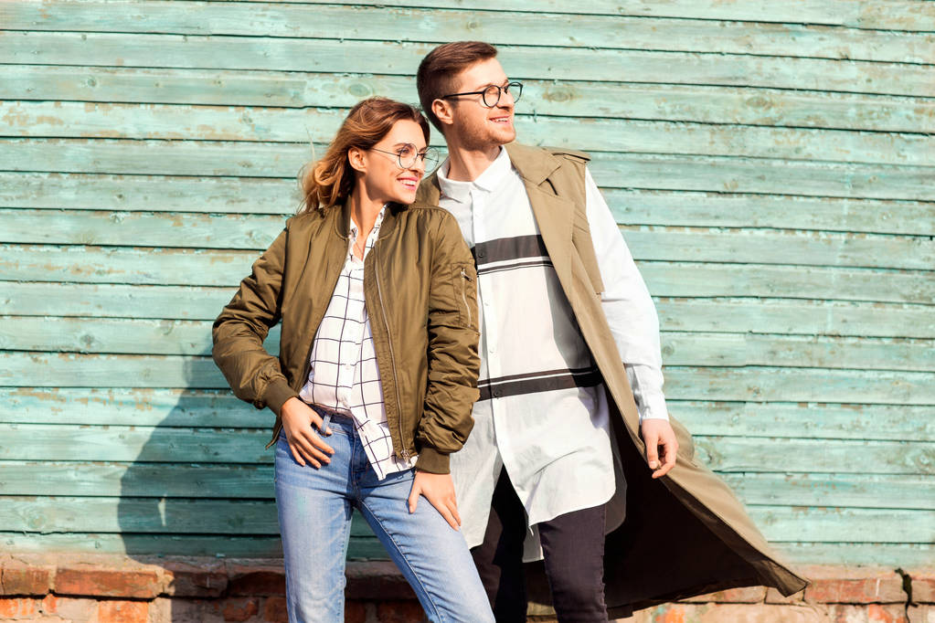 Módní pár v brýlích s brýle v zelených šatech pózuje na modré dřevěné zdi - Fotografie, Obrázek