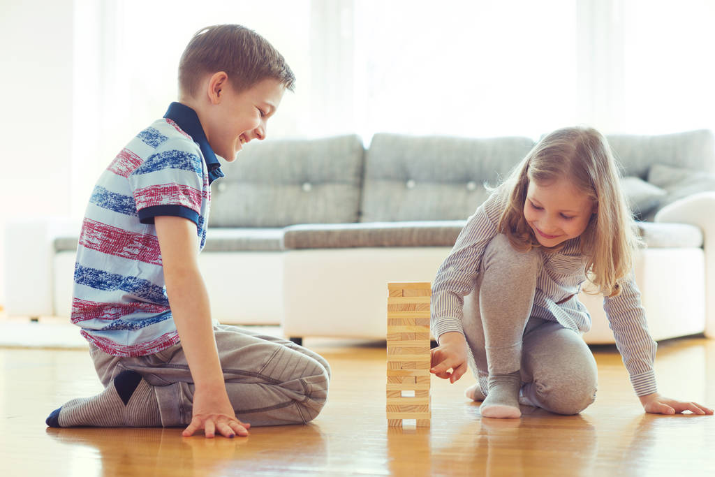 Двоє щасливих братів і сестер грають в гру з дерев'яними блоками вдома
 - Фото, зображення