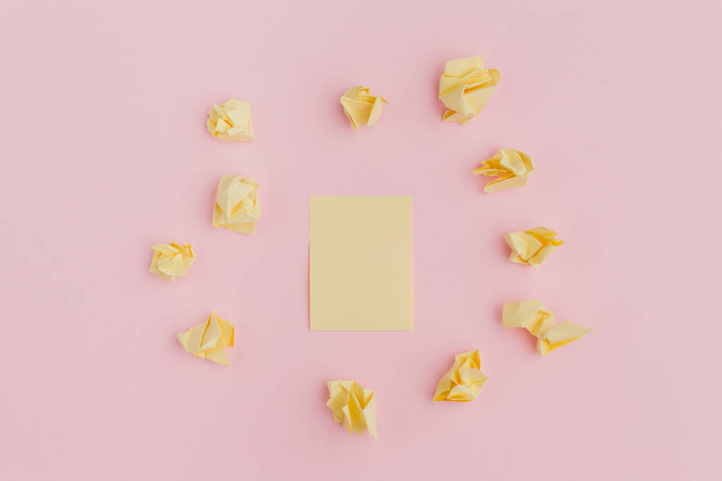 een stelletje verfrommeld gele stickers van papier, verspreid op een roze achtergrond, in het midden van een schone lei. Office-stijl - Foto, afbeelding