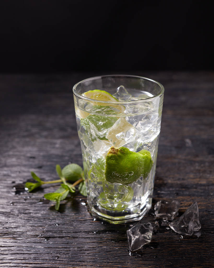 Glas geeister Mojito-Cocktail und Zutaten, Limette, Eis und Minzblätter auf schwarzem Hintergrund, kaltes Sommergetränk  - Foto, Bild