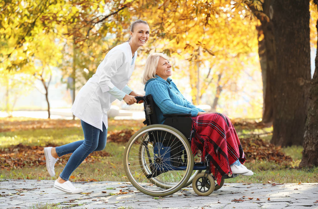 Старшая женщина-инвалид и молодая медсестра в парке
 - Фото, изображение