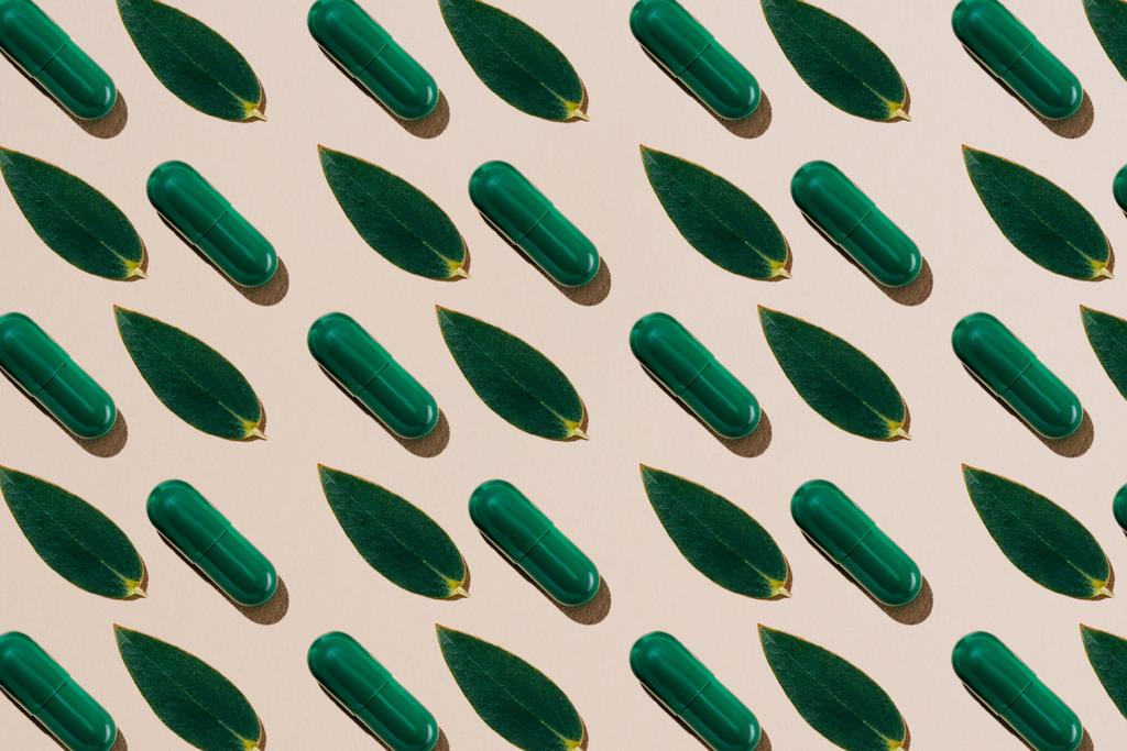 Ansicht von Phytotherapie-Pillen mit grünen Blättern im Reihenmuster auf beiger Oberfläche - Foto, Bild