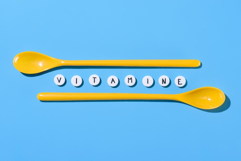 vista superior de cucharas de plástico amarillo y pastillas con letras de vitaminas en azul
 - Foto, imagen