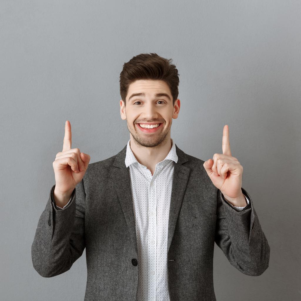 retrato de homem de negócios sorridente em terno apontando para a parede cinza
 - Foto, Imagem