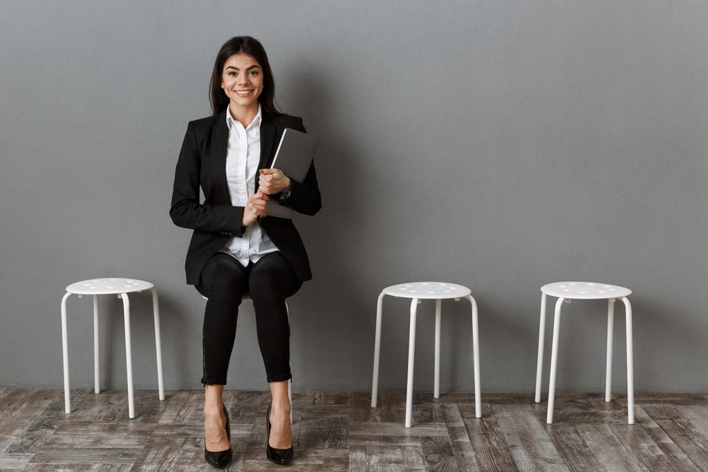 Glimlachende zakenvrouw in pak met laptop wachten op sollicitatiegesprek - Foto, afbeelding