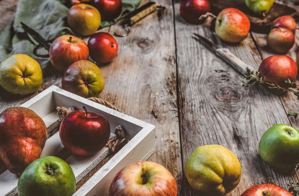 Close-up beeld van appels, peren, houten kist, mes, schaar, hand schalen en keuken handdoek op rustieke tafelblad - Foto, afbeelding